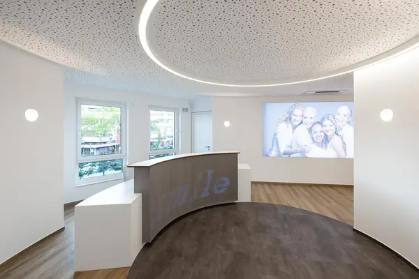 Heller Empfangsbereich einer Zahnarztpraxis mit modernem Tresen und großem Gruppenfoto.