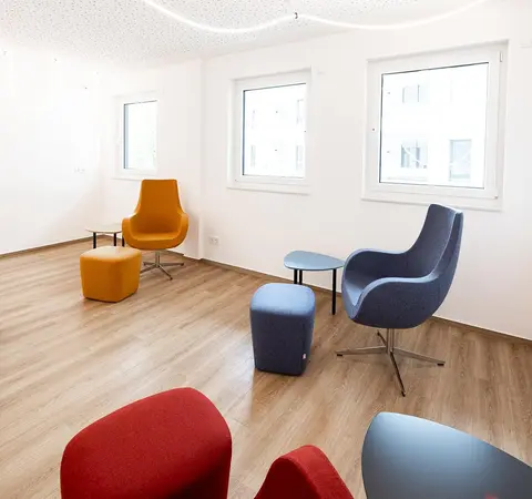 Moderner Wartebereich mit bunten Sesseln, Hockern und Holzboden in heller Umgebung.