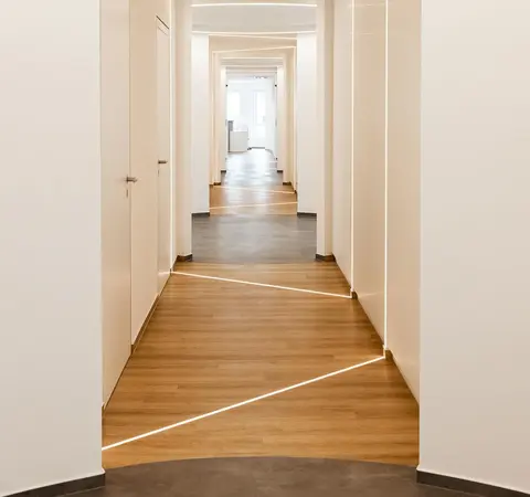 Moderner Flur mit Holzfußboden, weißen Wänden und integrierten LED-Lichtlinien im Boden.