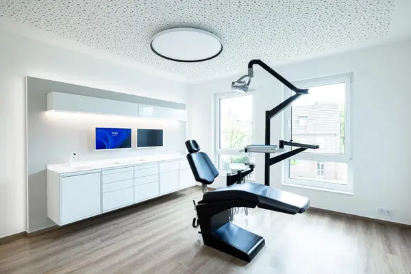Modernes, helles Zahnarztpraxis-Behandlungszimmer mit Behandlungseinheit und Monitoren.