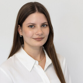 Junge Frau mit langen braunen Haaren im weißen Hemd vor neutralem Hintergrund, Portraitfoto.