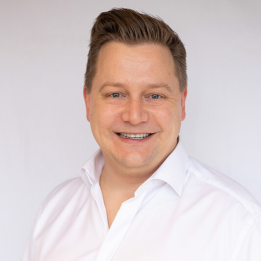 Porträt eines lächelnden Mannes im weißen Hemd vor neutralem Hintergrund für Business-Website.